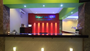A reception desk at Grand Inn Hotel with a red and green color scheme, a clock, and a digital display. - Grand Inn Hotel Mataram (Mataram)