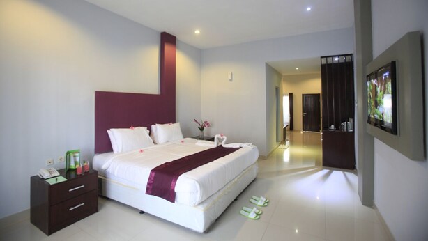 A modern hotel room with a large bed, a bedside table with a phone and toiletries, and a TV mounted on the wall. - Grand Inn Hotel Mataram (Mataram)