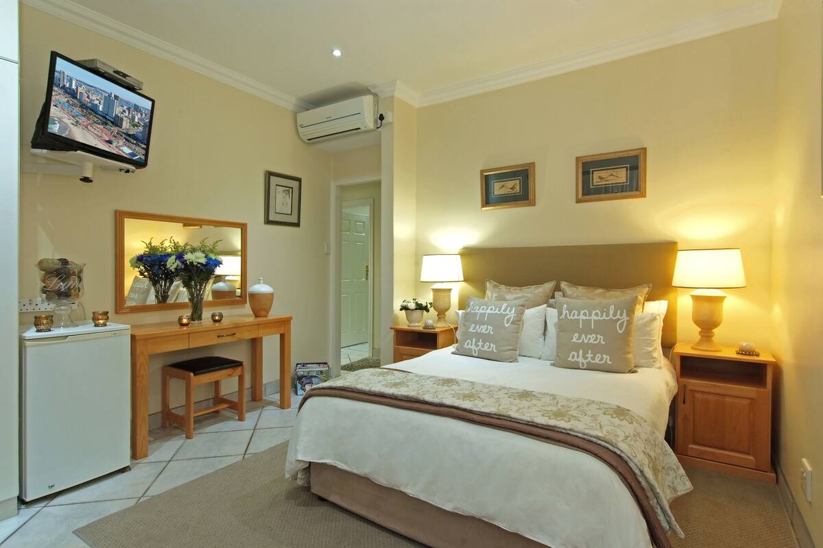 A hotel room with a large bed, bedside lamps, a desk with a mirror, and a television on the wall.