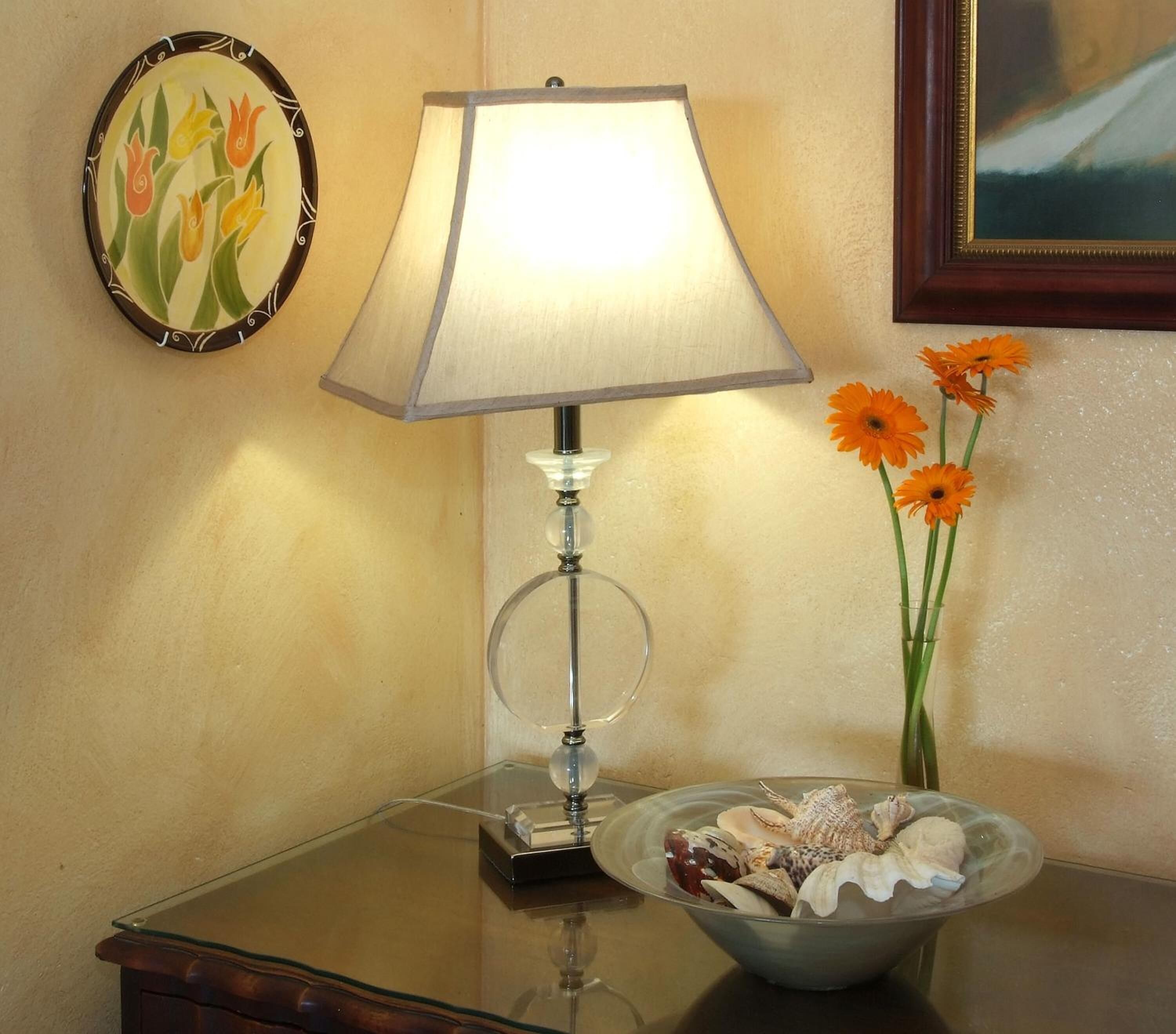 A table with a lamp, a bowl of seashells, and a vase with orange flowers.