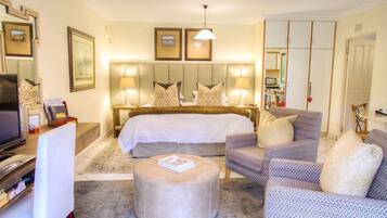 A hotel room with a large bed, two bedside lamps, a television, a desk, and a seating area with patterned chairs.