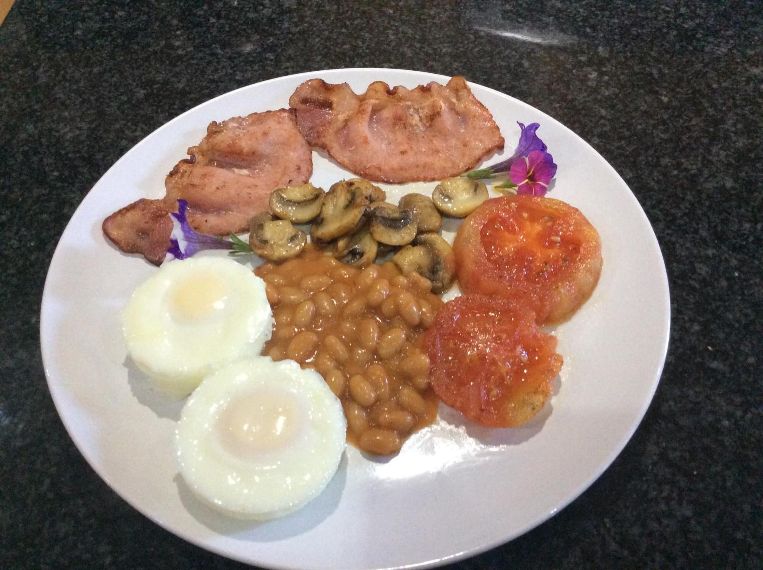 Ein Teller mit Speck, Pilzen, Baked Beans, Tomaten und zwei Spiegeleiern.