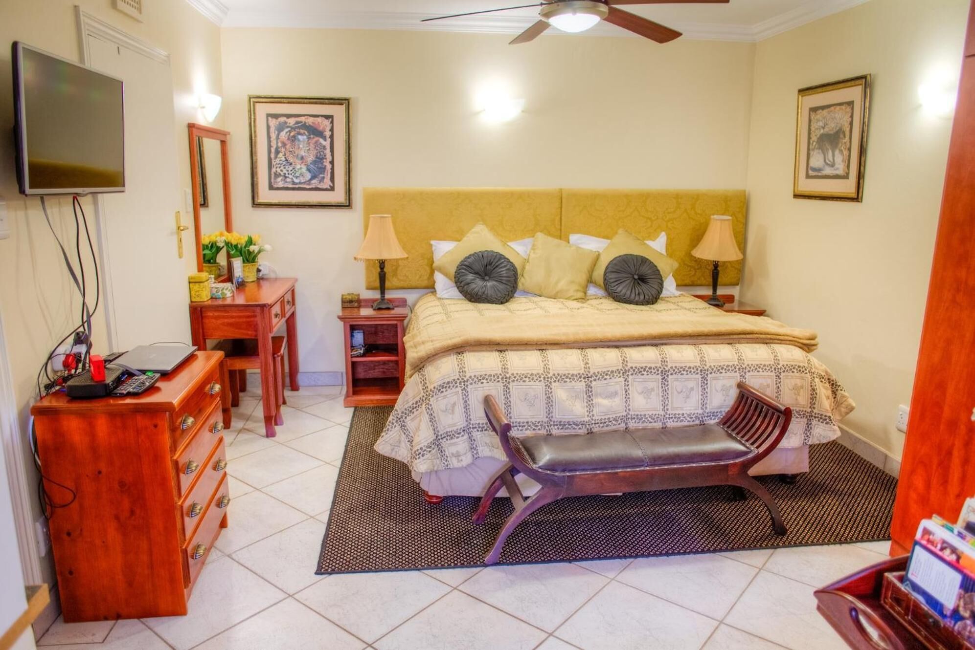 A bedroom with a bed, bedside tables, a desk, a chair, a television, and artwork on the walls.