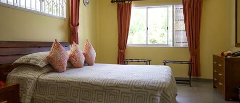 A bedroom with a bed, a dresser, a window with curtains, and a view of greenery outside.