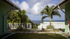 A view from a covered patio with a white fence, palm trees, and a clear sky.