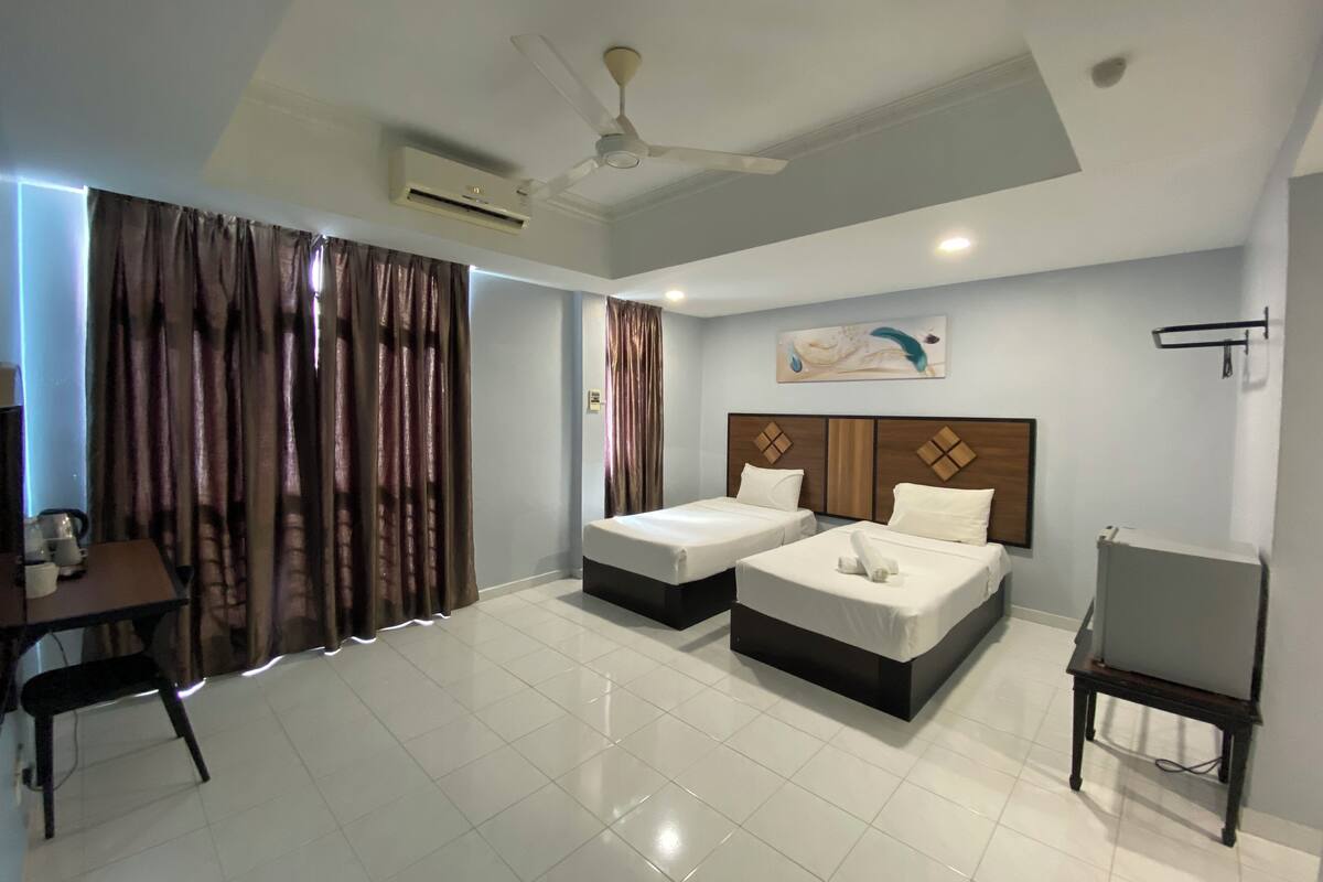 A hotel room with two beds, a desk, a chair, and a ceiling fan.
