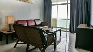 A modern hotel room with a sofa, a chair, a desk, a lamp, and a large window with curtains. - Leisure Cove Hotel & Apartments (George Town)