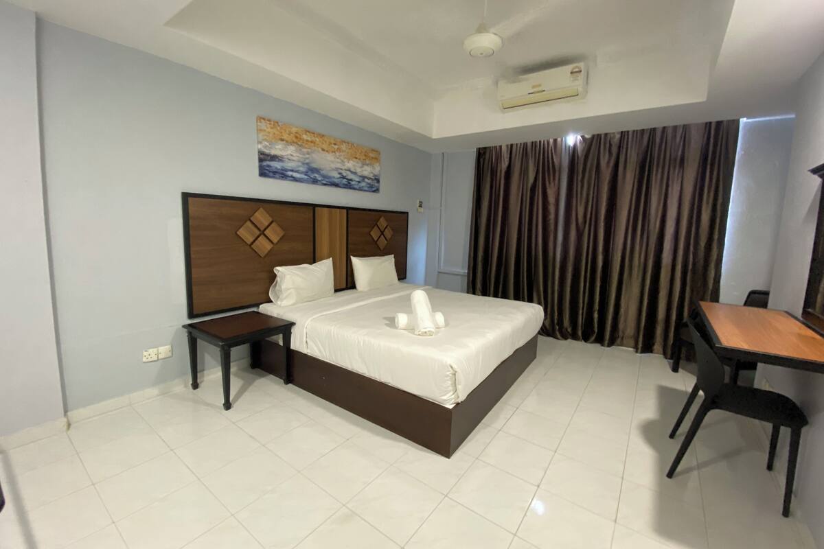 A hotel room with a large bed, a desk, and a chair. There is a ceiling fan and an air conditioning unit.
