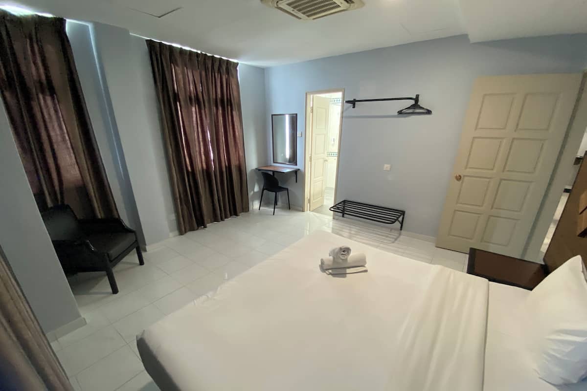 A hotel room with a large bed, a desk, a chair, a TV, and a door.