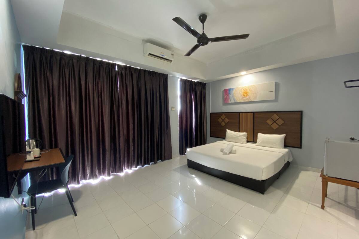 A modern hotel room with a large bed, a ceiling fan, and a desk with a chair.