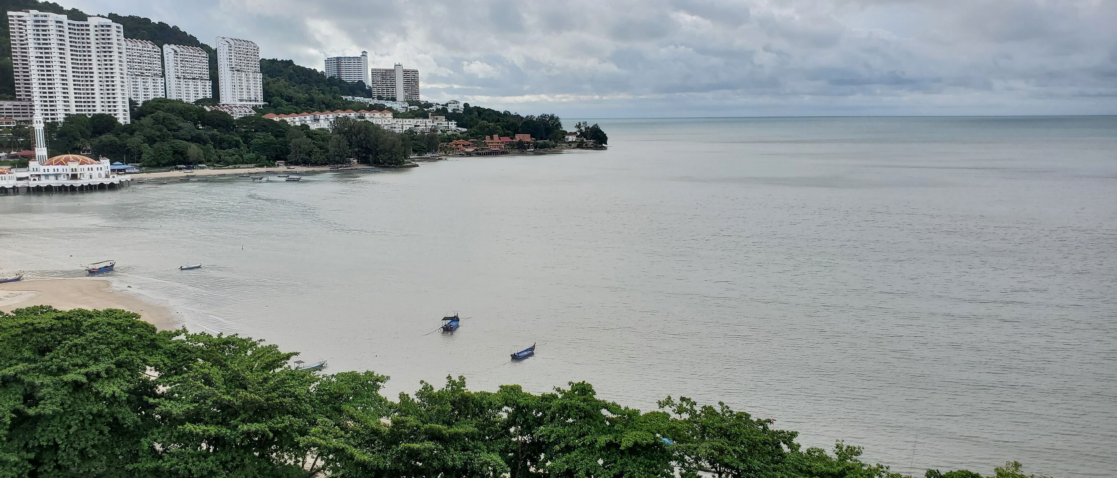 Un paysage urbain côtier avec de hauts immeubles, une plage et des bateaux sur l’eau.