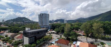A high-rise building with a modern glass facade, surrounded by lush greenery and a mountainous backdrop.