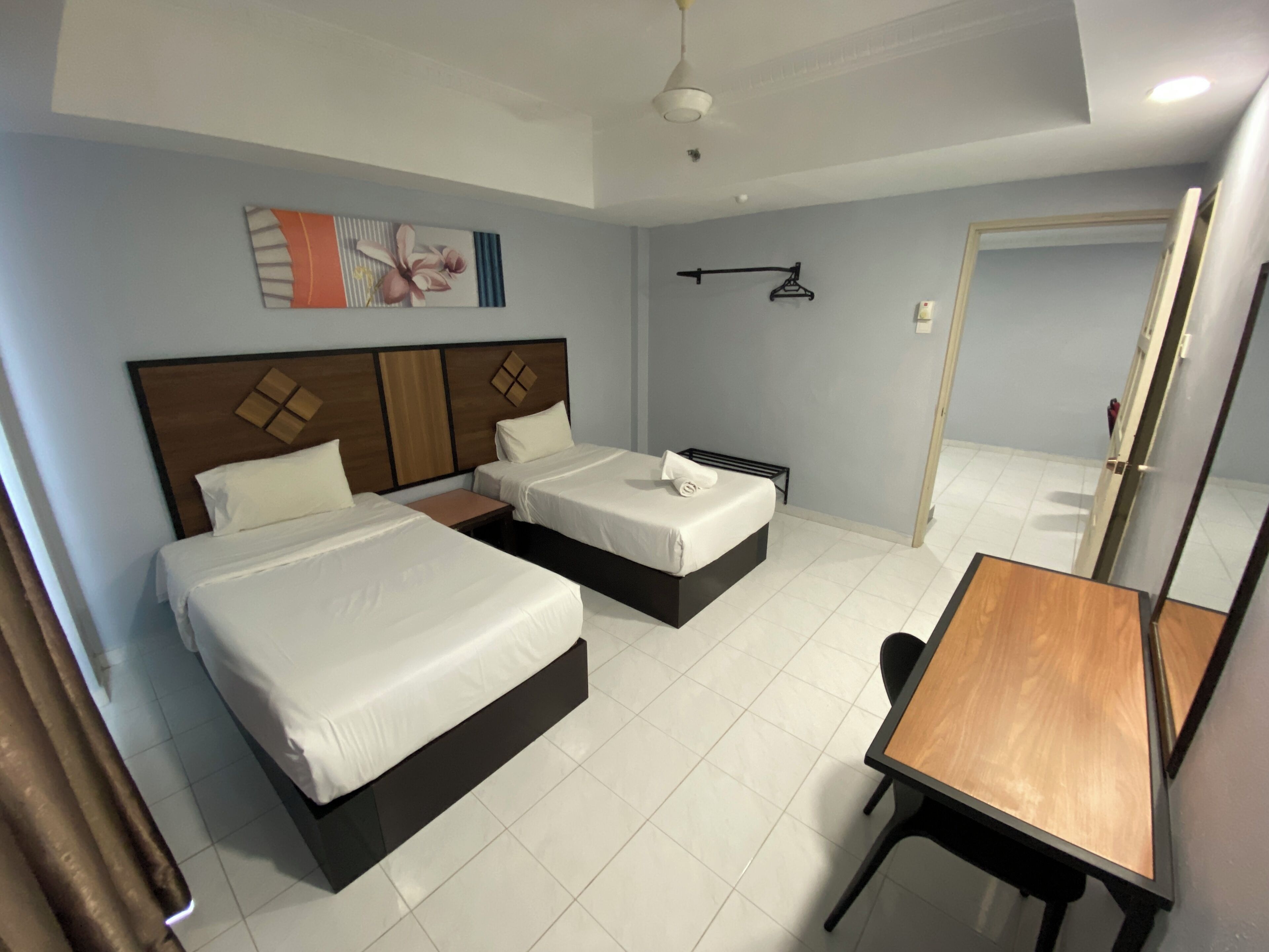 A hotel room with two beds, a wooden desk, and a hanging coat rack.