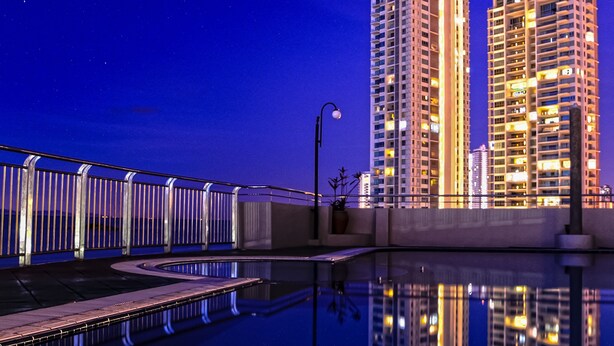 A nighttime view of two high-rise buildings with illuminated windows, reflecting on a calm body of water. - Leisure Cove Hotel & Apartments (George Town)