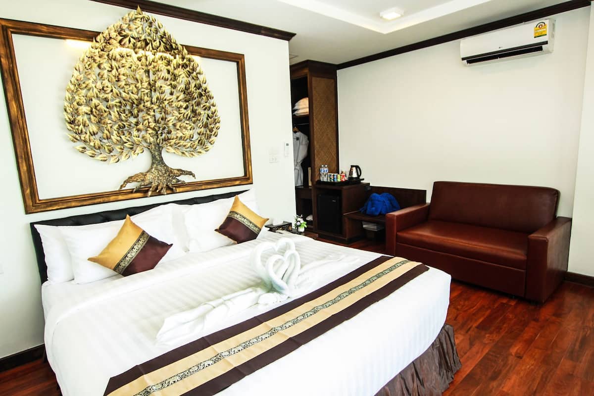 A hotel room with a large bed, a brown leather sofa, a wall-mounted air conditioner, and a framed artwork above the bed.
