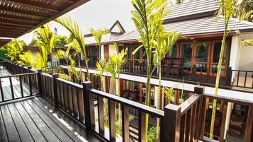 A wooden deck with a railing, surrounded by potted plants and overlooking a building with large windows and a balcony.