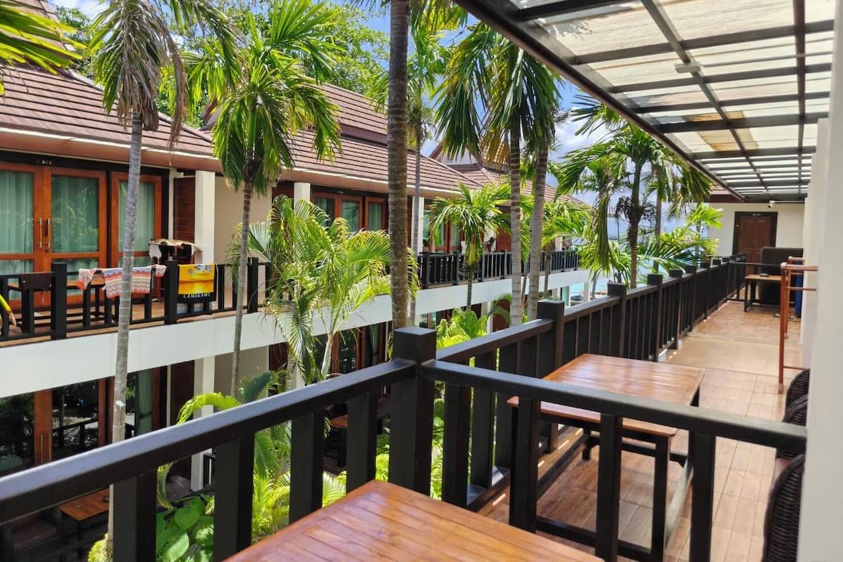 A hotel with a covered outdoor seating area, multiple floors, and palm trees.