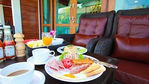 A breakfast setting with a wicker table, a glass of orange juice, a plate of eggs, bacon, and ham, and a bottle of Heinz ketchup. - Cabana Lipe Beach Resort (Koh Lipe)
