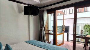 A hotel room with a bed, a TV mounted on the wall, and a sliding glass door leading to an outdoor area with a table and chairs. - Cabana Lipe Beach Resort (Koh Lipe)