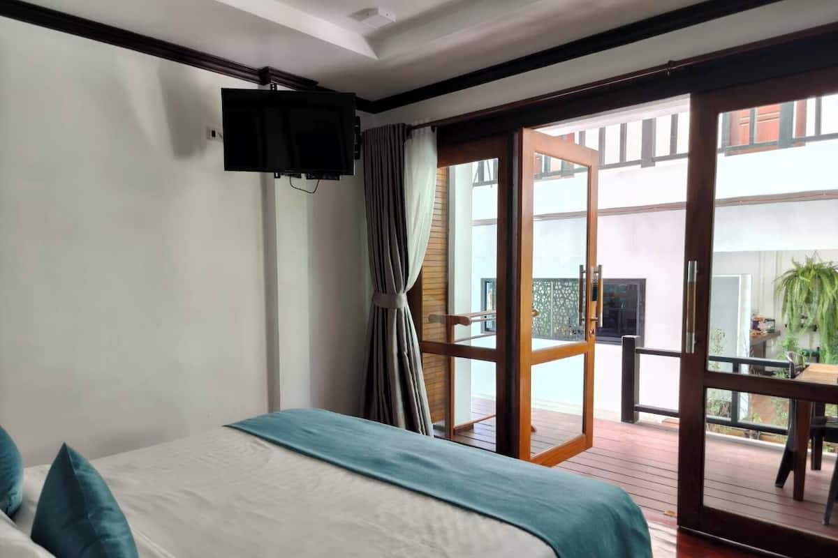 A hotel room with a bed, a TV mounted on the wall, and a sliding glass door leading to an outdoor area with a table and chairs.