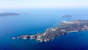 An aerial view of a coastal area with a densely forested peninsula, clear blue waters, and several small islands. - Le Domaine de la Mer (Hyères)