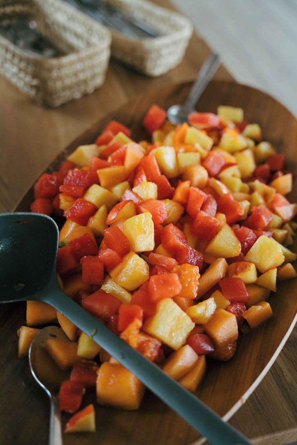 A wooden cutting board with diced fruits, a knife, and a bowl.