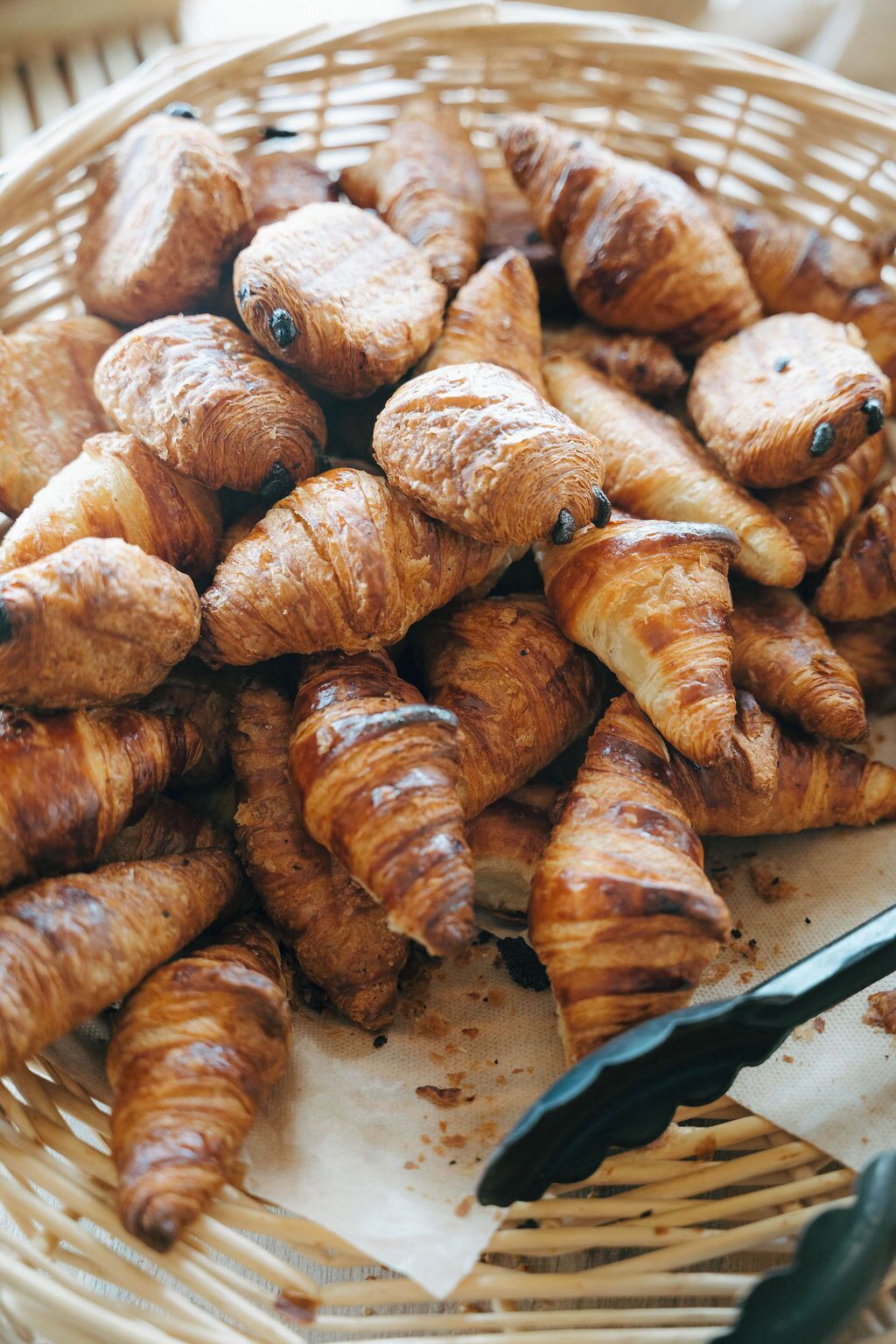 A basket filled with assorted pastries, likely croissants, placed on a surface with a piece of parchment paper.