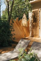 A wooden deck with two lounge chairs, a thatched umbrella, and a wooden fence.