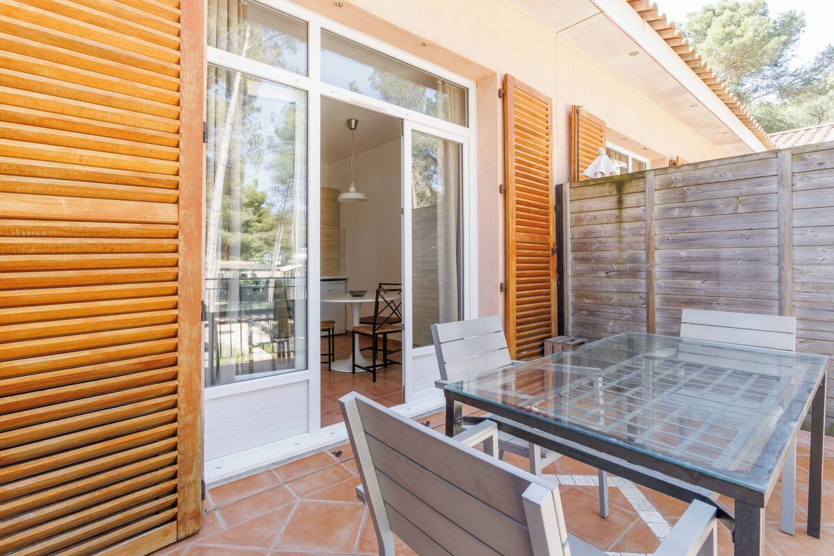 A glass-top table with chairs, a wooden fence, and a sliding glass door leading to an interior space with a kitchen and dining area.