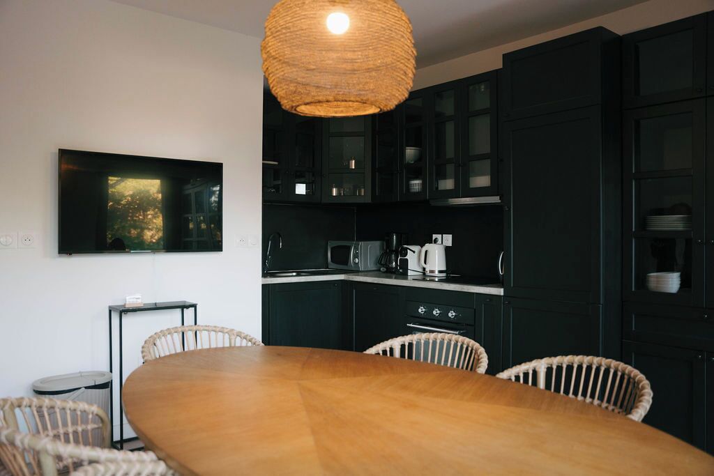 Eine moderne Küche mit dunklen Schränken, einem Holztisch, Korbstühlen und einer Pendelleuchte.