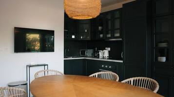 Eine moderne Küche mit dunklen Schränken, einem Holztisch, Korbstühlen und einer Pendelleuchte.
