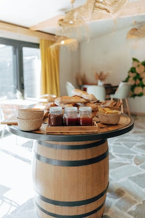 A wooden barrel table with a tray of bread, jars of jam, and woven baskets.