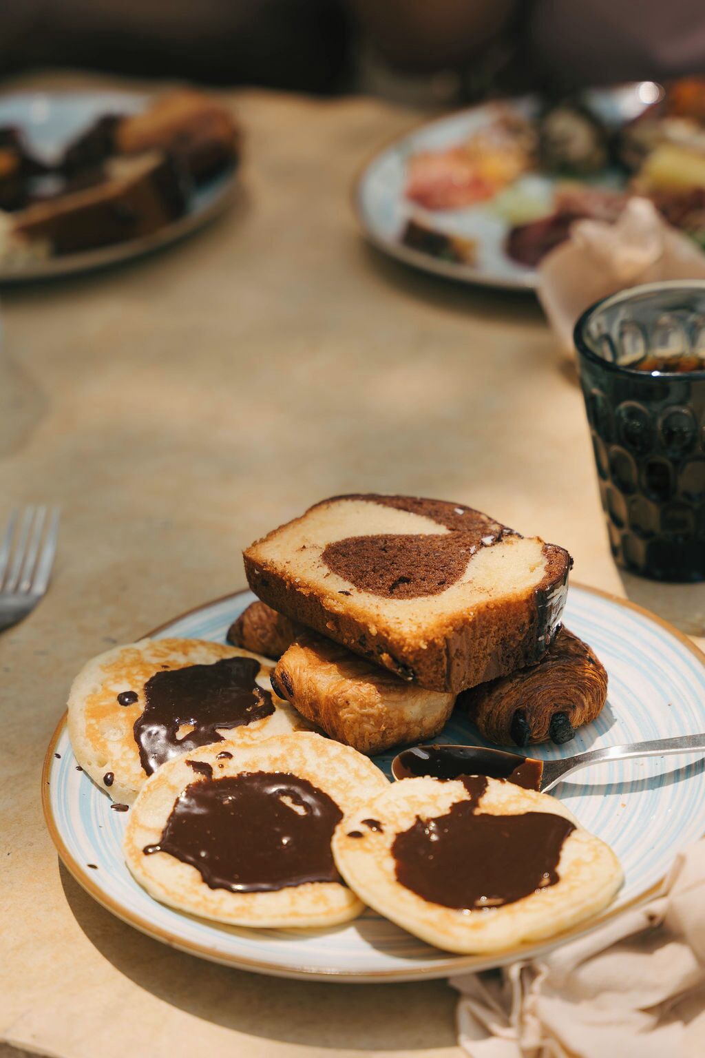 Desayuno con tortitas, una rebanada de pastel y un vaso de una bebida oscura sobre una mesa.