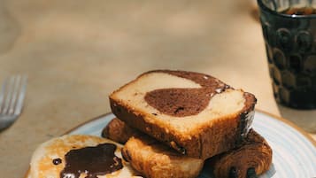 Ein Frühstückstisch mit Pfannkuchen, einem Kuchenstück und einem Glas dunklem Getränk.
