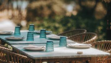 A table set outdoors with wicker chairs, a white tablecloth, and blue glass candle holders.