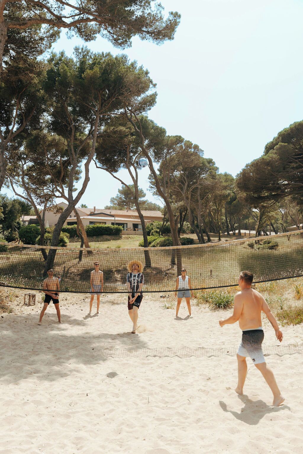 Un espacio al aire libre con arena, una red de voleibol, árboles y un edificio al fondo.