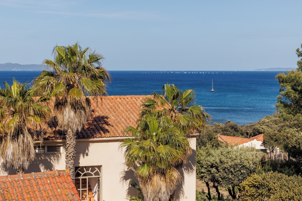 A coastal view with a building featuring a tiled roof and palm trees.