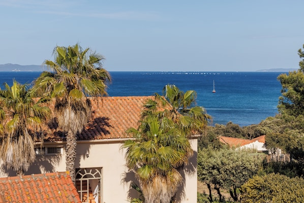 A coastal view with a building featuring a tiled roof and palm trees. - Le Domaine de la Mer (Hyères)