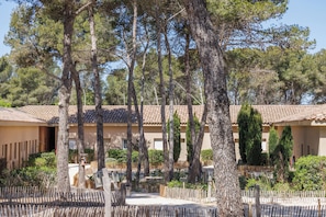 A courtyard with tall trees, a tiled roof, and a wooden fence. - Le Domaine de la Mer (Hyères)