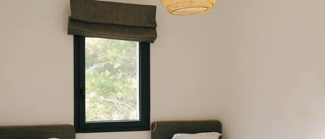 A bedroom with two single beds, a window with a view, and a hanging light fixture.