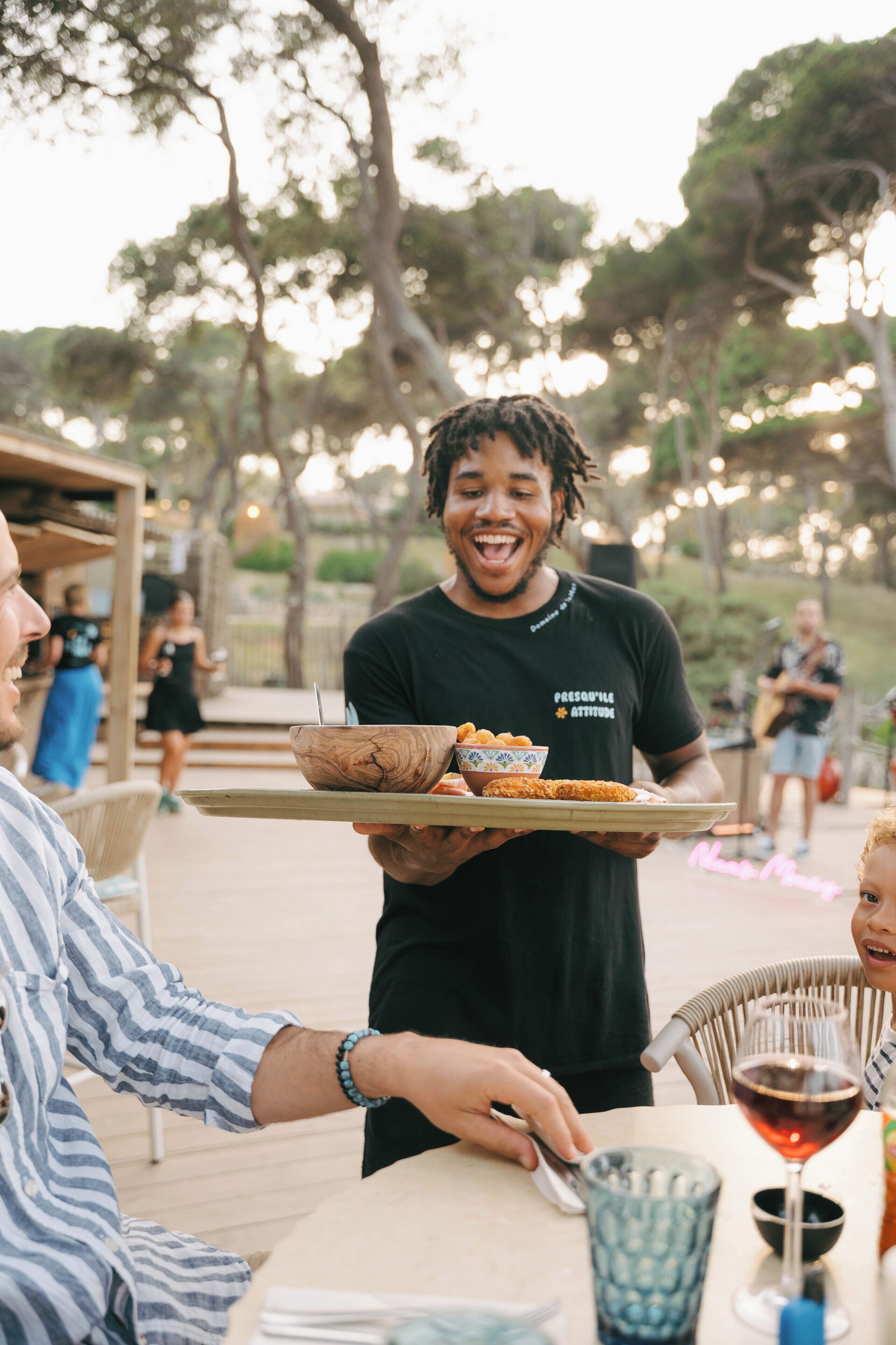 A person serving food at an outdoor dining area with a casual atmosphere.
