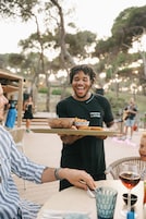 A person serving food at an outdoor dining area with a casual atmosphere.