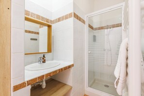 A bathroom with a white sink, a mirror, and a glass-enclosed shower. - Le Domaine de la Mer (Hyères)