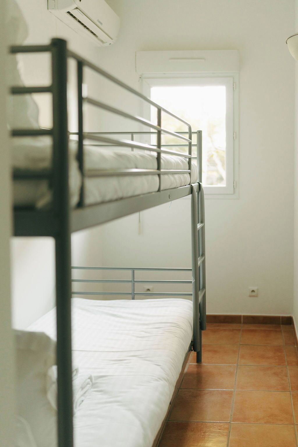 A bunk bed room with a window and a wall-mounted air conditioner.