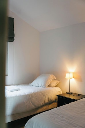 A single bed with white bedding and a bedside table with a lamp.