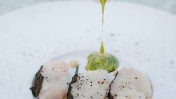 Une main verse une sauce verte sur un plat contenant du poisson et des légumes.