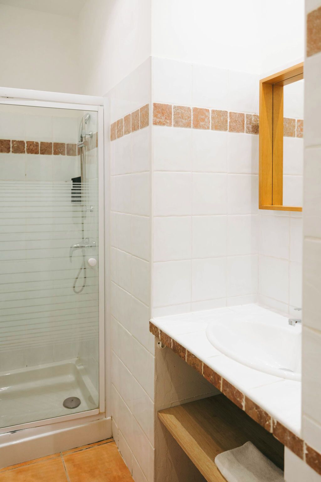 Une salle de bain avec une douche à parois de verre, des carreaux blancs, un plan de toilette en bois et un miroir.
