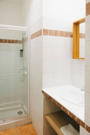 A bathroom with a glass-enclosed shower, white tiles, a wooden countertop, and a mirror. - Le Domaine de la Mer (Hyères)