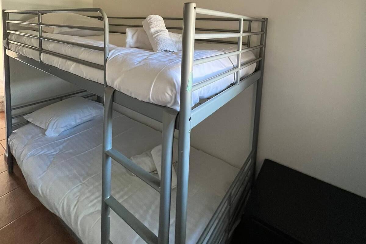 A bunk bed room with a metal frame, white bedding, and an air conditioning unit on the wall.