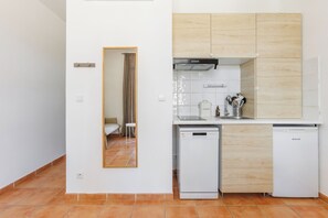 A compact kitchen with white cabinets, a dishwasher, and a compact refrigerator. - Le Domaine de la Mer (Hyères)